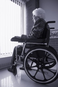 Senior Woman On Wheelchair Looking Out Of Window With Blinds